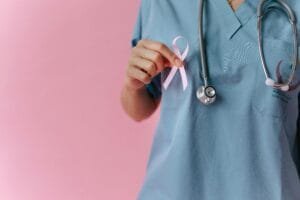Healthcare worker in scrubs holds a pink breast cancer awareness ribbon symbolizing support.